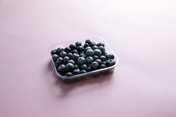 Plastic container with fresh raw organic ripe blueberries on a pink background
