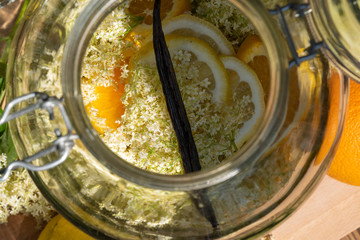 View from above directly into the big preserving jar with the fresh elderflowers, oranges and lemon slices and the vanilla pod for the elderflower liqueur