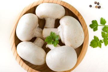 A bunch of fresh porcini mushrooms in a wooden bowl on a white background with parsley and pepper. The view from the top.