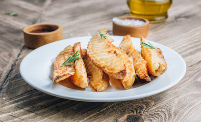 Baked potato fries with sea salt and rosemary on a rustic wooden background.