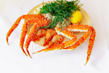 Shrimp, crab, lemon and greens on a plate on a white background.