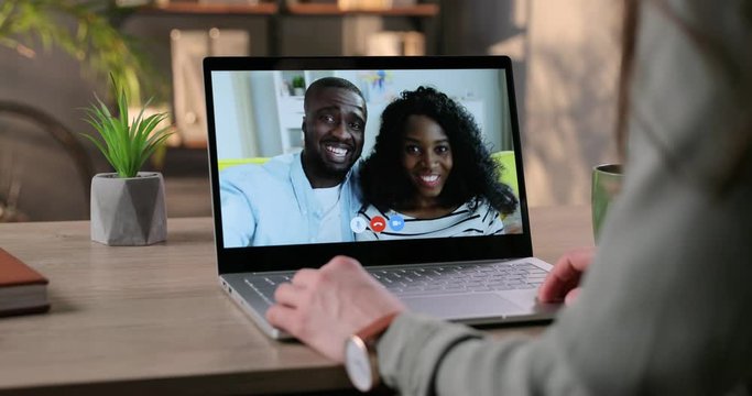 Girl sitting in room and video chatting on laptop with joyful African American couple at home. Female having video conversation with smiling friends through webcam and waving her hand. Chat concept