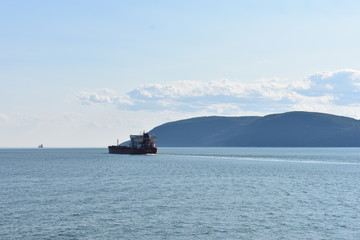 Boat in ocean with mountains in the background and clouds in the sky