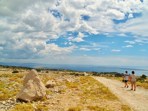 Typical czech tourists walking on tour in dry stony landscape on the top of hill on island Rab with sea view and clouds over horizon during summer holidays, active vacation