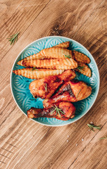 Chicken drumsticks with french fries on blue plate on rustic wooden table.