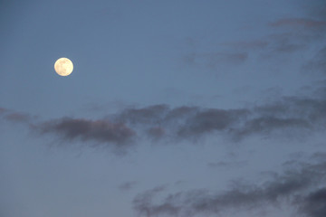 A bright round full moon in the night sky surrounded by wispy clouds.