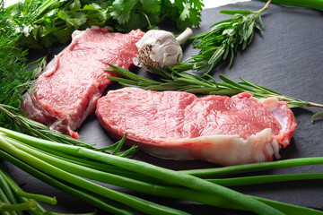 Raw meat. Two slices of fresh raw meat, a branch of rosemary and garlic on a black slate stone plate. Preparing meat for a barbecue.