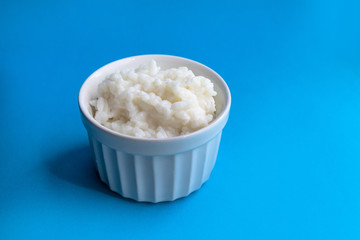 Tasty rice porridge in a white bowl on blue background. Proper healthy eating breakfast concept.