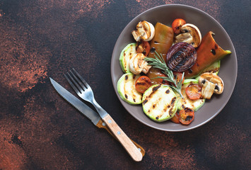 Grilled vegetables (zucchini, cherry tomatoes, onions, champignons, bell peppers) served in a plate with rosemary and sea salt on a dark vintage background. Top view. Copy space