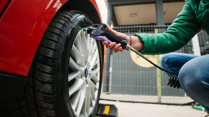 Young woman who takes care of the tires of the car spraying tire protectant solution in self car...