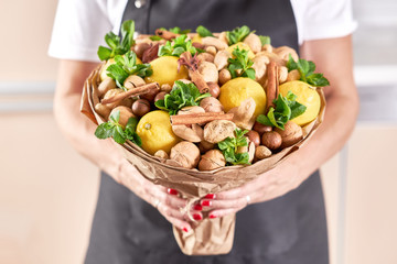 A large beautiful fruit bouquet of lemons, nuts, ginger and mint in the hands of a woman florist
