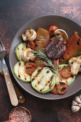 Grilled vegetables (zucchini, cherry tomatoes, onions, champignons, bell peppers) served in a plate with rosemary and sea salt on a dark vintage background. Top view. Copy space. Vertical