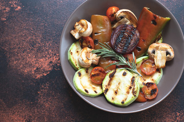 Grilled vegetables (zucchini, cherry tomatoes, onions, champignons, bell peppers) served in a plate with rosemary and sea salt on a dark vintage background. Top view. Copy space
