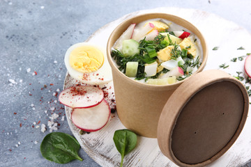 Summer okroshka soup. Soup with radish, egg, dill, potatoes and sour cream on white wooden board on grey table. Food for delivery. Background image, copy space
