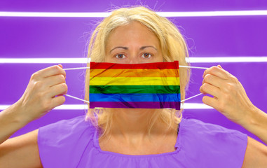 Woman with a rainbow flag on a surgical mask. Concept of the outbreak and quarantine for coronavirus pandemic in the LGBT community.