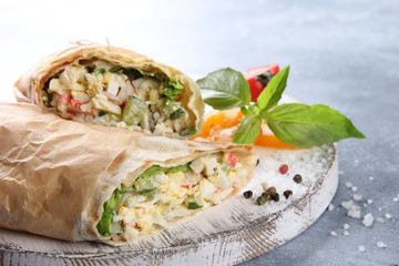 Pita bread with crab sticks, cucumbers, eggs and lettuce on white wooden board on grey table. Rolls in parchment, cherry tomatoes, herbs, spice. Shawarma, wrap. Background image, copy space