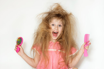 a little girl with tangled long hair in a pink dress on a white background. stands with two combs in different hands and does not know what to do