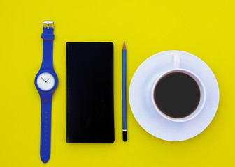  White cup of coffee, pencil, notebook, hand watch on yellow background