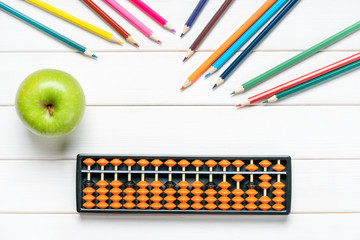 Abacus for number calculation, pencils and green apple on white wooden desk. Mathematics learning,...