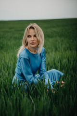 Fototapeta premium A young woman sits among the field of wheat.