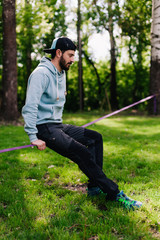 portrait of a young, athletic, bearded guy in a blue hoodie near slackline
