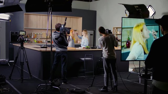 WIDE Behind the scenes of studio set, makeup artist make corrections during shooting television cooking show featuring female chef, professional TV production. Shot on ARRI Alexa Mini