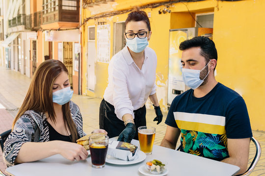Clients with masks on the terrace of a bar in Spain attended by a waiter with gloves and masks. Social distancing during phase one of de-escalation. Coronavirus