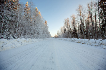 Empty snowy forest road at sunset  