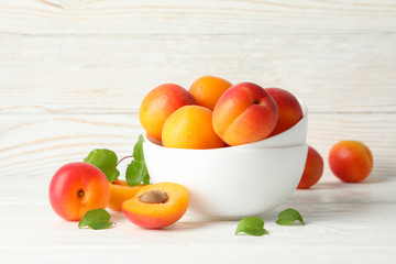 Bowl with tasty apricots on white wooden background
