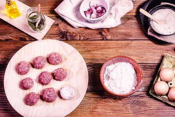 Raw meatballs, flour and ingredients on a wooden base. Home cooking concept.