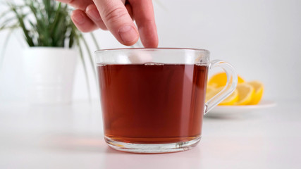 Putting sugar cubes in glass cup hot tea. Close up.