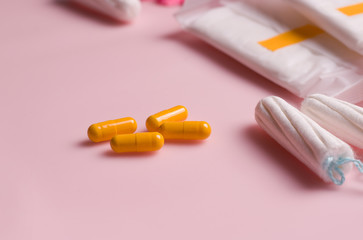 Menstrual pain pill concept. Panty liners and tampons next to yellow capsules on a pink background. Copy space