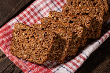 against a dark background fresh whole-grain dark bread sliced ​​and neatly laid out on a red cloth. nutritious, healthy product consisting of grains and dried fruits for a healthy and tasty lifestyle.