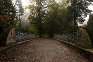 South Moravia, Kromeriz. Beautiful, gloomy atmosphere of autumn. An old ornate wrought iron bridge over it leads the way to the park. Around the bridge are tall green trees.