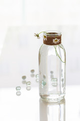 Three daisy flowers embedded in a glass vase tied with natural twine. The vase is full of water and stands on a white table. There are small transparent balls around the bottom.