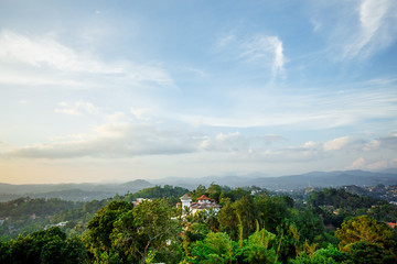 White villa on a hilltop amidst tropical trees against a mountain background
