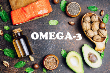 Animal and vegetable sources of omega-3 acids as salmon, avocado, linseed, nuts, almonds, chia seeds, spinach and olive oil on dark background. Top view. flat lay. Lettering - Omega 3 - obrazy, fototapety, plakaty
