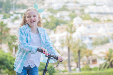 Active little toddler girl riding scooter on road in park outdoors on summer day.  Summer time fun