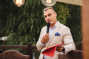 Presenter with a microphone in his hands holds an event and smiles.