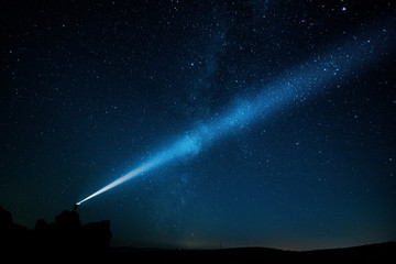 Night landscape of a man with a powerful military flashlight illuminating the starry sky leaving a...