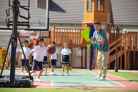 Foreign teacher and children playing basketball in playground