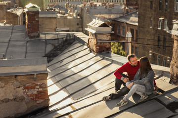 Fototapeta premium A date on the roof of the house. Lovers in the city of romance. Walk on the roof of the city. Young couple husband and wife are sitting on the roof cuddling.