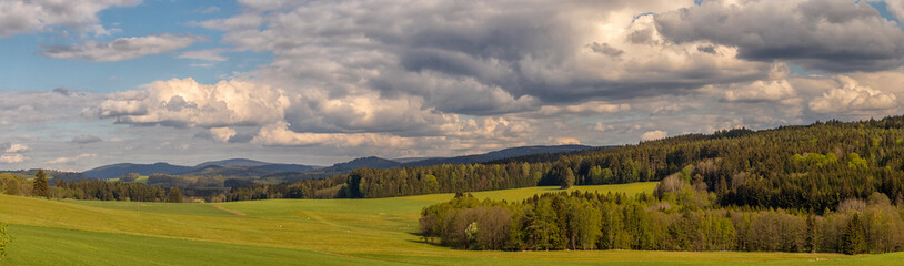 beautiful landscape with meadows, trees, forests, in the background wooded hills and blue sky with white clouds