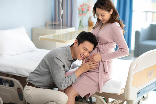 Husband listening to his pregnant wife's belly in hospital ward