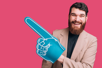 bearded man wearing jacket and a blue fan foam glove on pink background.