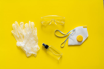 Respirator ffp, rubber gloves, antiseptic and protective glasses lie on a yellow background. Anti-virus protection kit against covid-19. Coronavirus pandemic 2019.