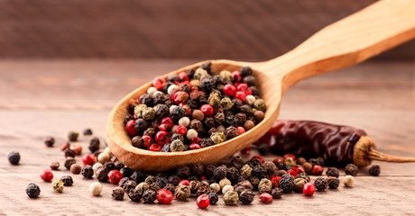 Mix peppercorns in spoon on wooden background