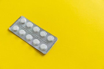 Top view on the pills in the package. White pills on yellow background. Medicine, medication, painkillers, tablet, medicaments, drugs, antibiotic, vitamin, treatment, capsule, dose. Pharmacy theme.