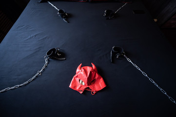 BDSM equipment. Top view of a red leather devil mask and black handcuffs with chains on a gray...