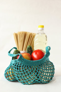 Set of products: apples, cucumbers, spaghetti, vegetable oil, canned food for cooking in a green bag-string bag on a white background, vertical frame